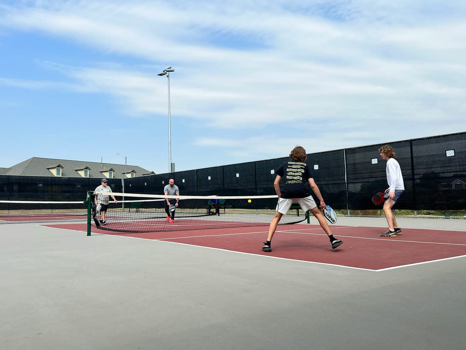 Four players in the middle of an outdoor pickleball doubles match on a red and grey court