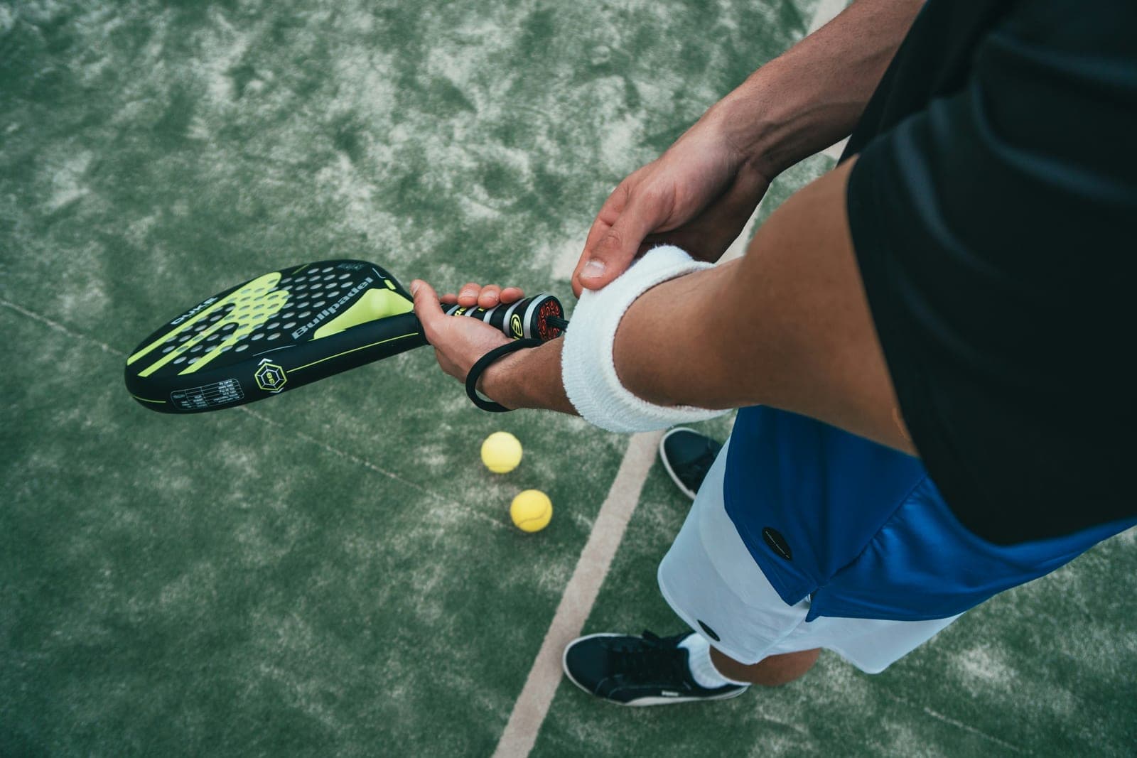 Player putting on a white wristband while holding a yellow and black Bullpadel padel racket on a green court