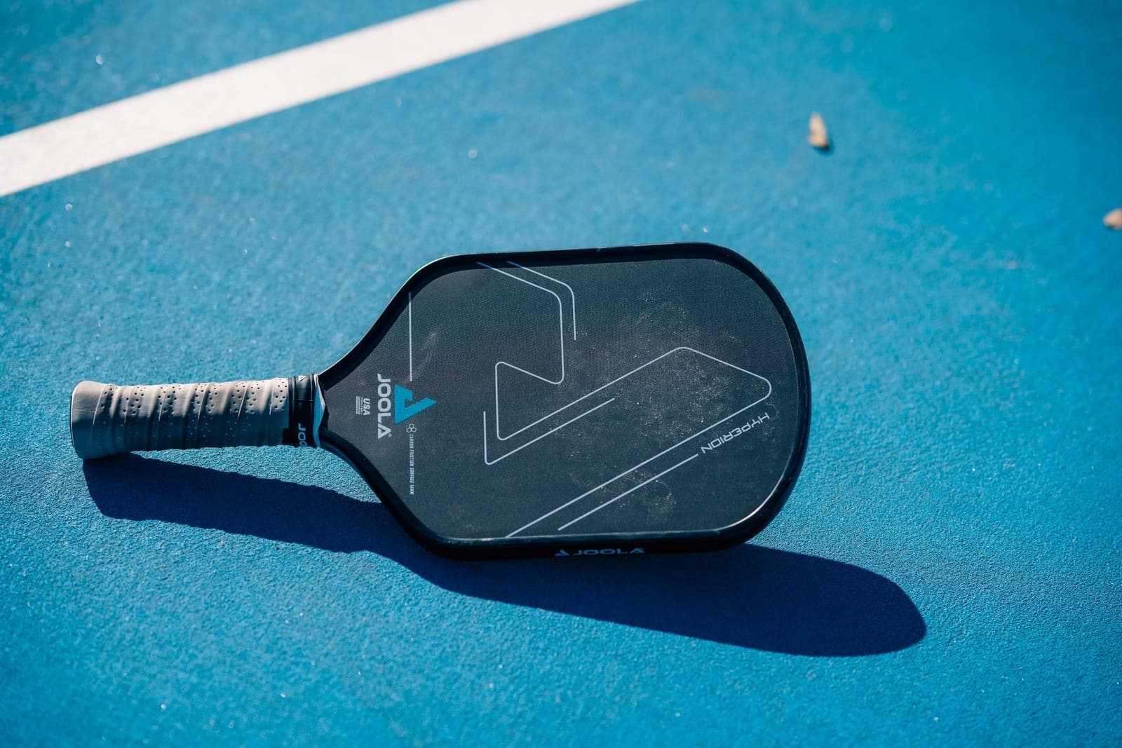 JOOLA Hyperion pickleball paddle on a blue outdoor pickleball court surface in low sunlight